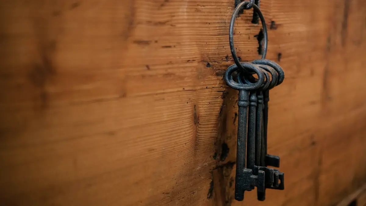 Un trousseau de clés anciennes accroché au mur, sur un fond de bois clair.