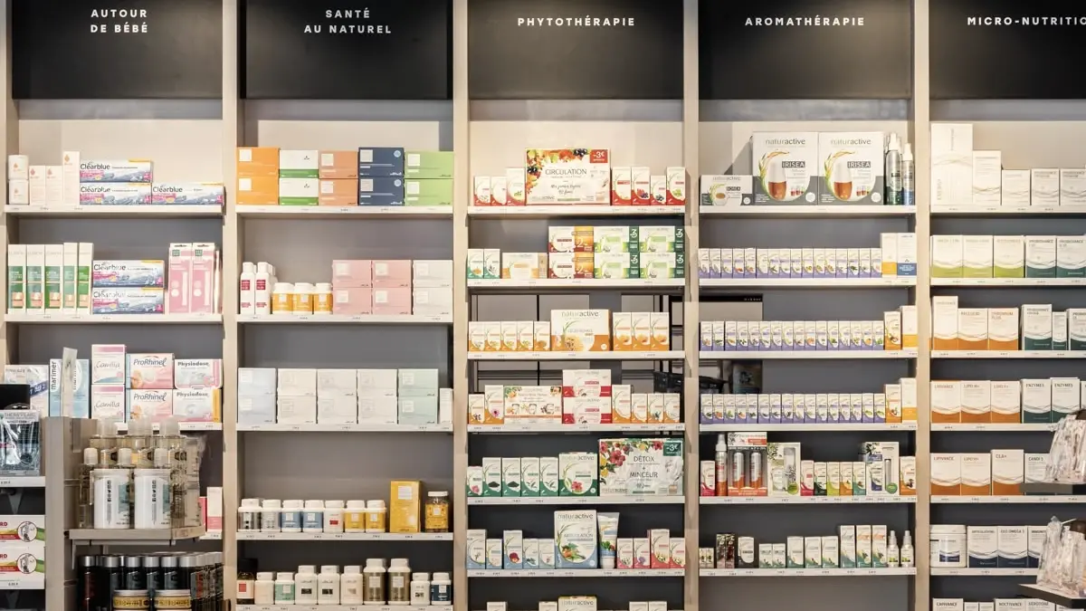 Les rayonnages d'une pharmacie contemporaine, bandeaux noirs légendés au-dessus des étagères de bois clair.