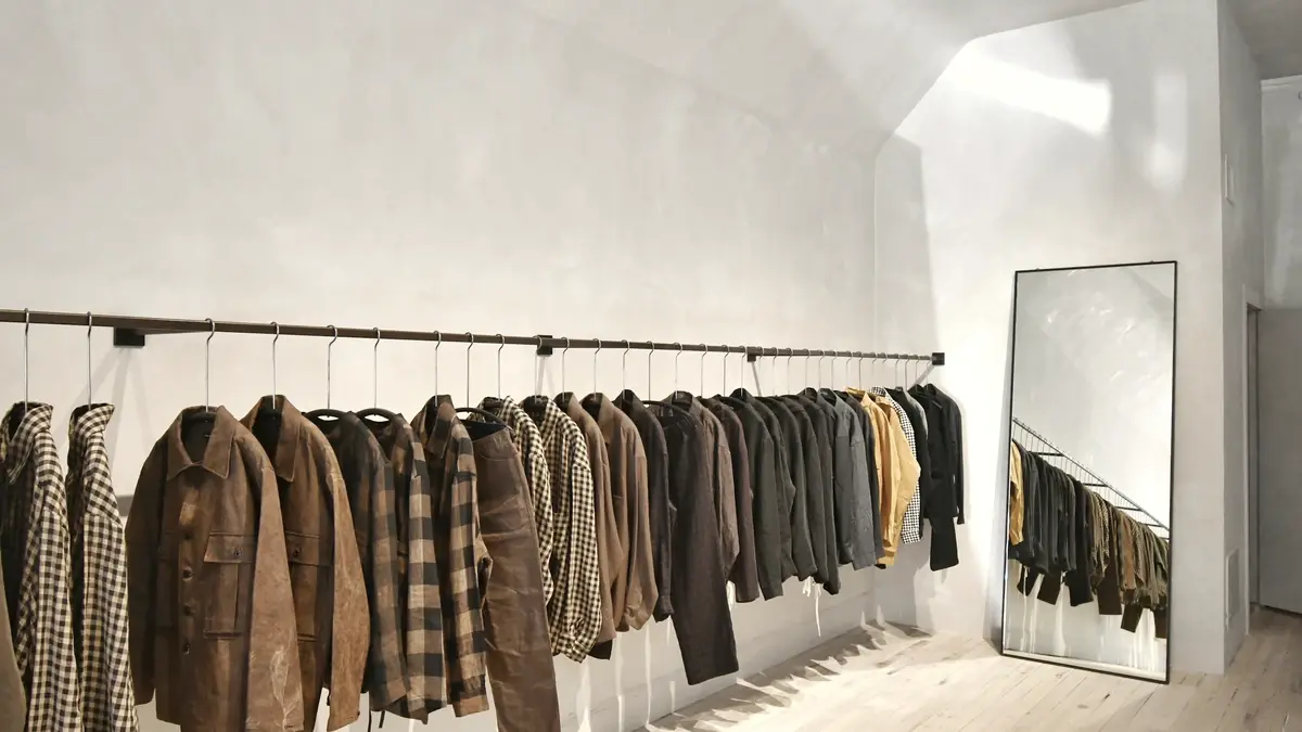 Un portant de manteaux dans une boutique claire, face à un miroir posé au sol.