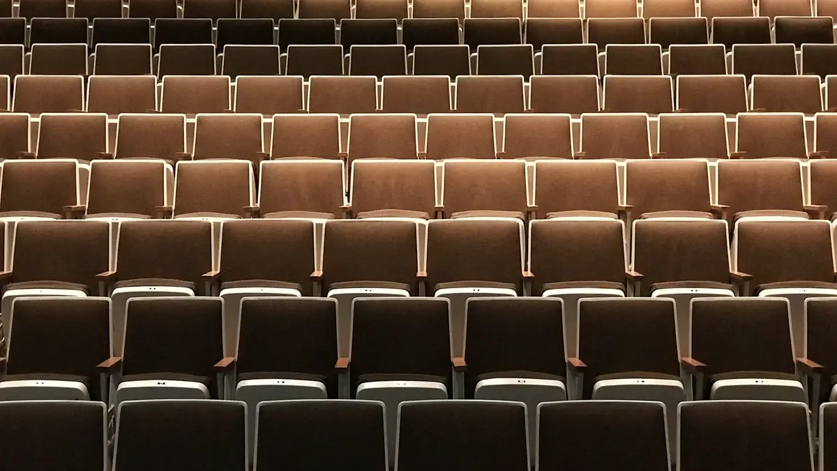 Des rangées de fauteuils de théâtre identiques et vides, sous une lumière ambrée.