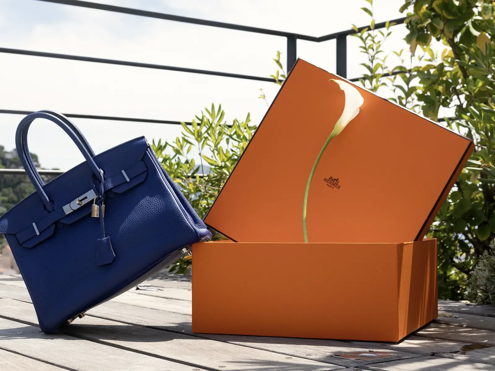 Un sac à main de luxe posé près de sa boîte orange, sur la table d'une terrasse.